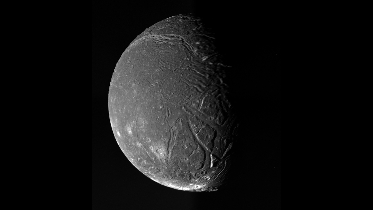 A grayscale image of a ridged and cratered moon with only the left hemisphere illuminated.