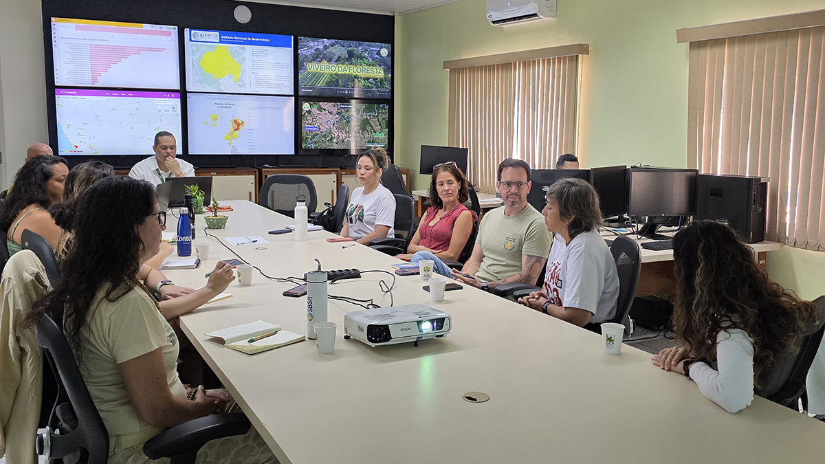 People sit around a conference table with satellite maps of the Brazilian state of Acre projected on a screen.