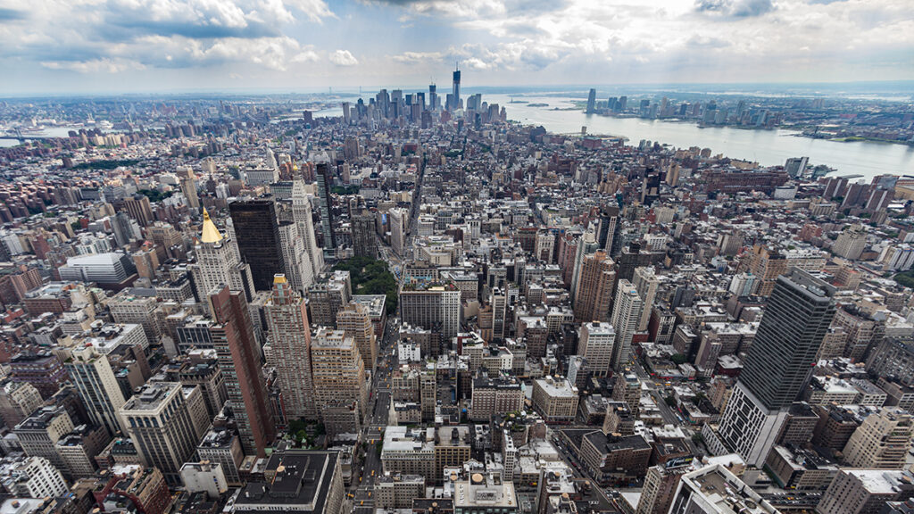 An aerial view of Lower Manhattan in New York City showing a dense collection of skyscrapers, traffic on streets, and some water surrounding the island