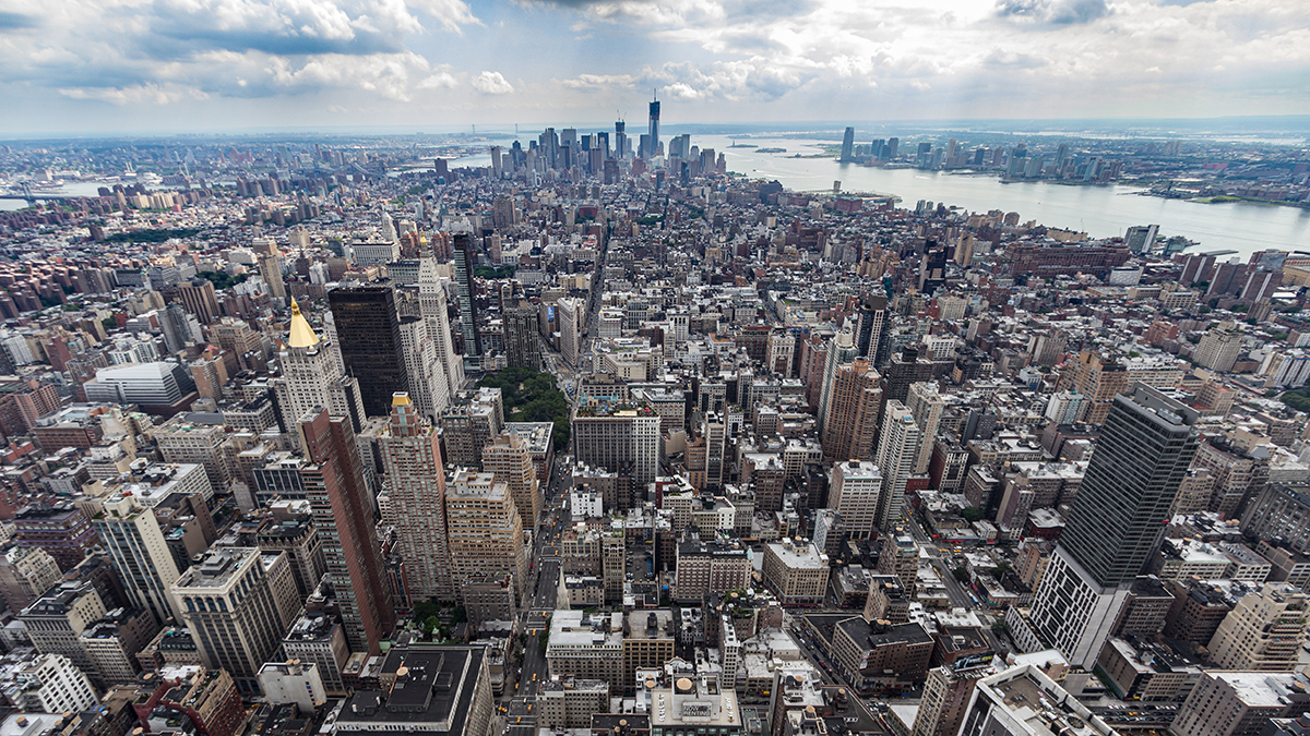 An aerial view of Lower Manhattan in New York City showing a dense collection of skyscrapers, traffic on streets, and some water surrounding the island