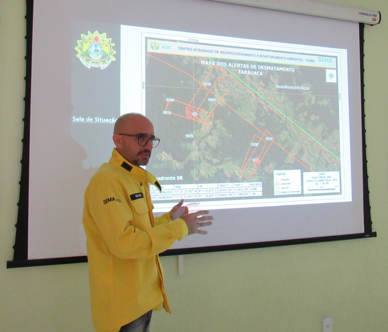 Quelyson Souza, a bald man in a yellow jacket, explains a slide projected on a wall.