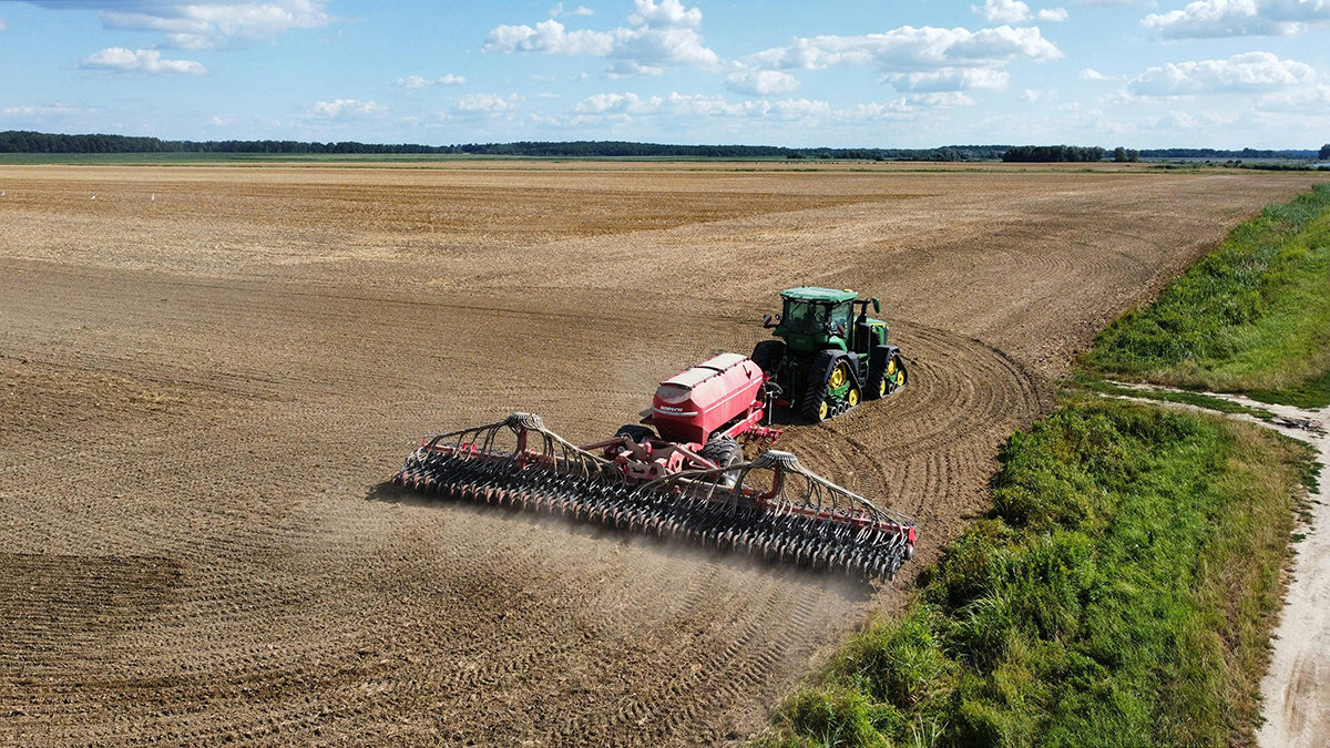 Aerial view of a green tractor pulling a red seeder across an large unplanted farm plot