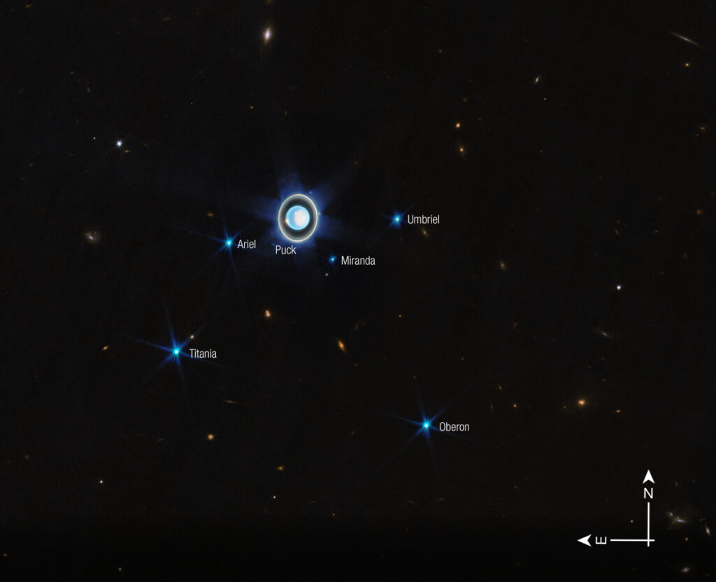 A nearly face-on image of Uranus that showcases its complex ring system and several major moons. The image labels the moons Oberon, Titania, Umbriel, Miranda, Puck, and Ariel.