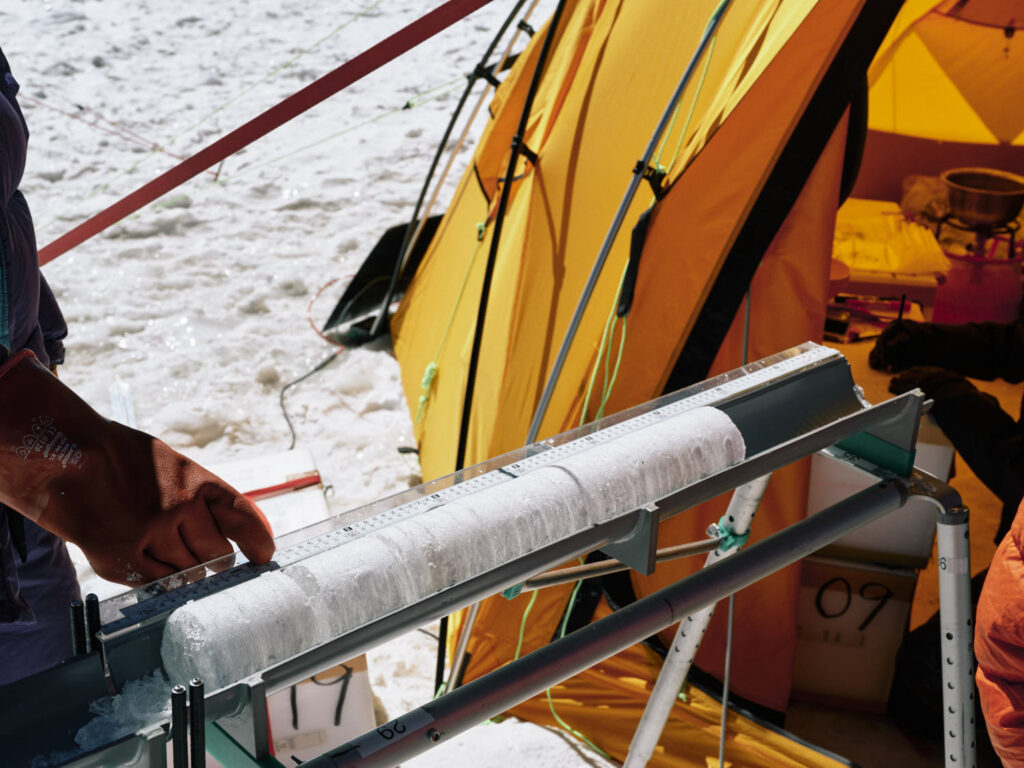 A cylinder of ice sits in a specially made cradle next to an orange tent.