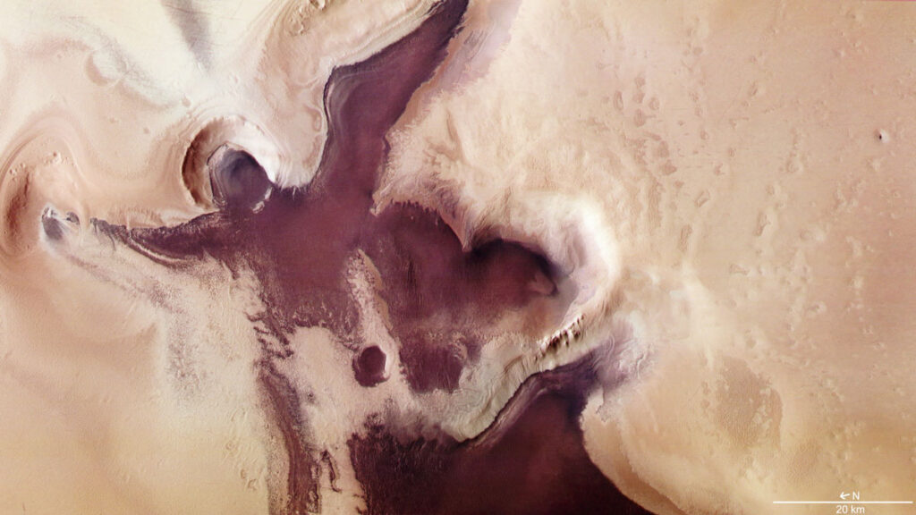 A satellite image shows dark sand deposits near the south pole of Mars. The shape formed by the deposits is reminiscent of an angel with outstretched wings with a large heart under its right wing.