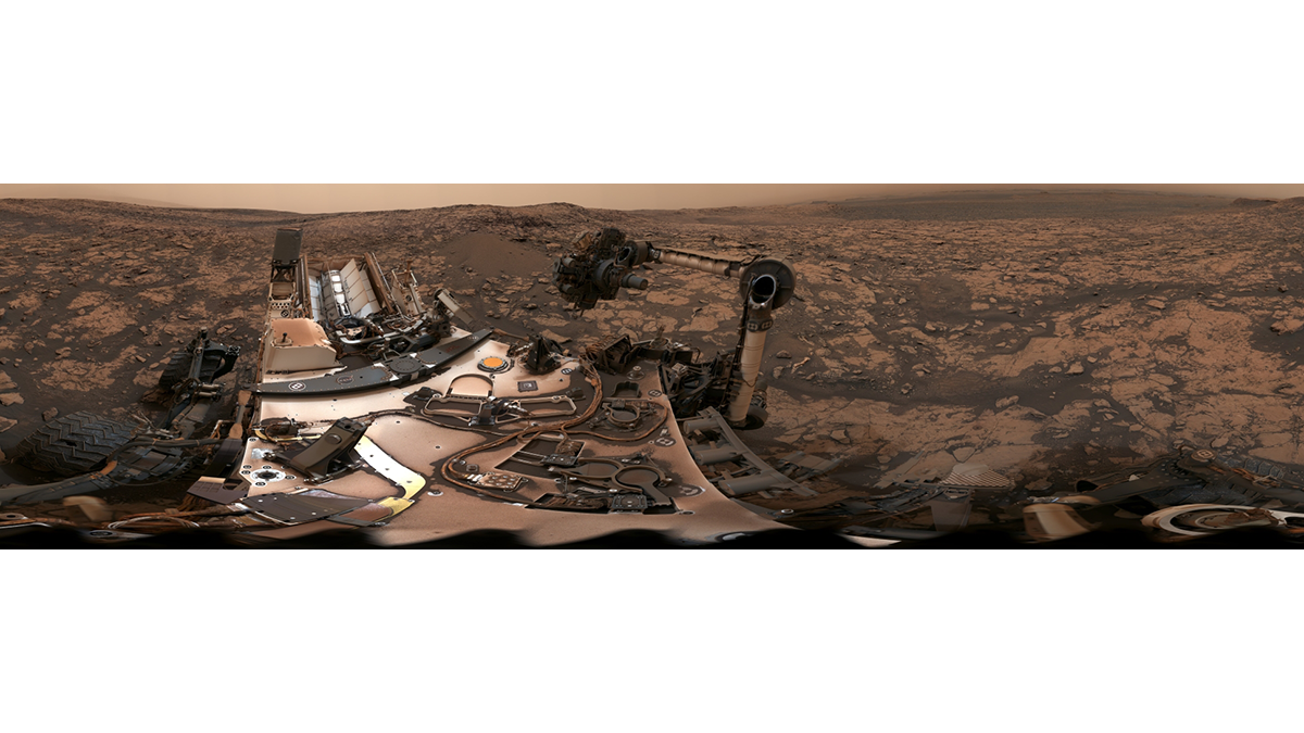 A rover sits atop a rocky ridge on Mars, under pink skies.
