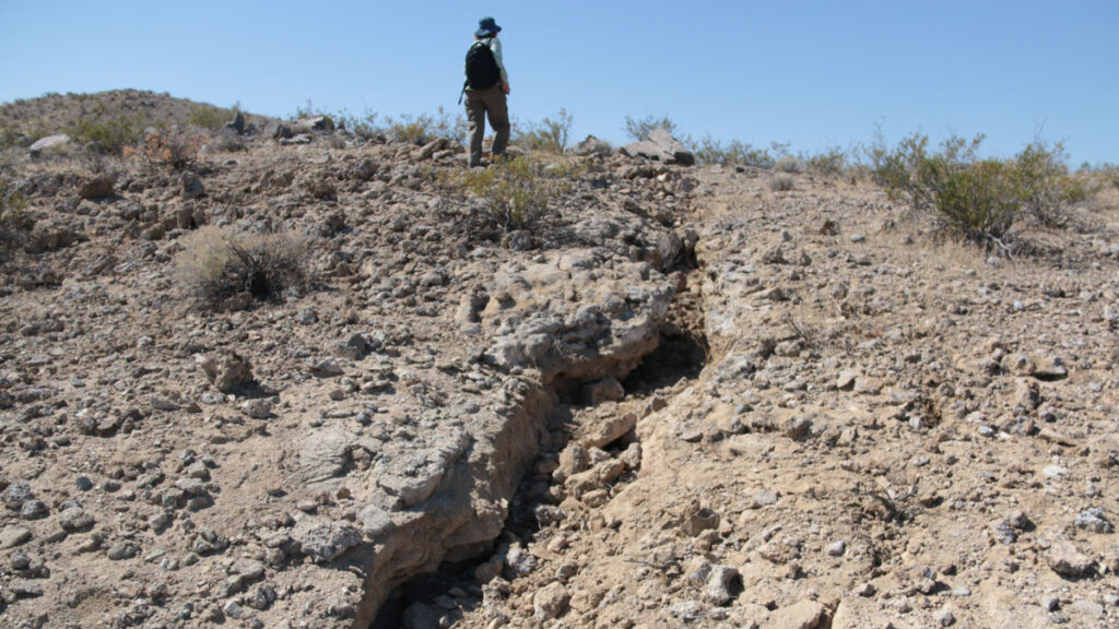 A rupture in the rocky soil extending at an angle with a researcher in the top middle of the image.