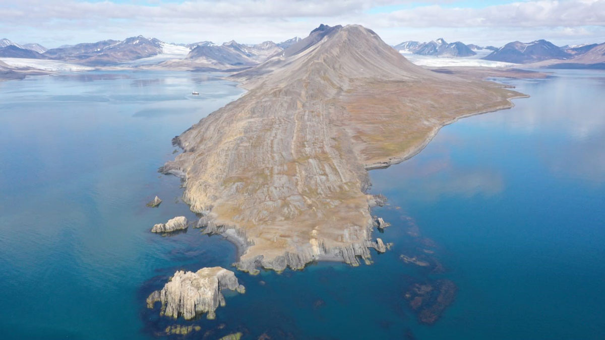 A drone image of a piece of mountainous land jutting out into the blue ocean.