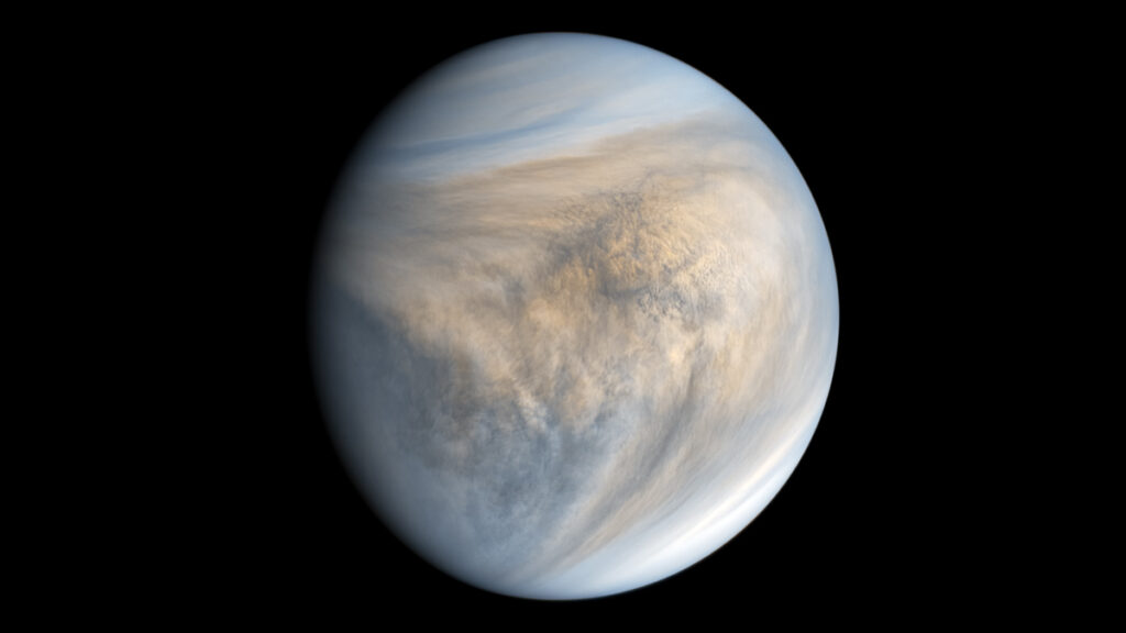 The planet Venus appears as a circular shape against a black background, with the right side sharply defined but the far left side fading into shadow. White, gray, and light orange swirling shapes cover the surface, appearing whiter, more linear, and more solid at the top and bottom of the circle but patchier toward the middle, with more patches of gray and light orange.