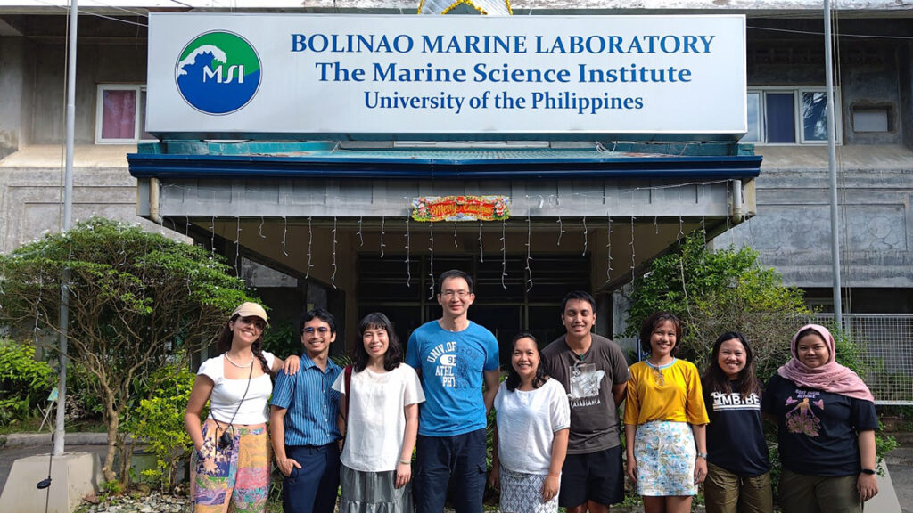Nine researchers pose for a photo outside a concrete building with a sign reading “Bolinao Marine Laboratory, The Marine Science Institute, University of the Philippines.”