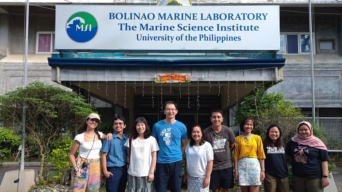 Nine researchers pose for a photo outside a concrete building with a sign reading “Bolinao Marine Laboratory, The Marine Science Institute, University of the Philippines.”