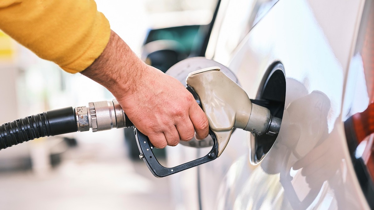 A close-up image shows a hand holding a gas pump that is releasing gas into a white car.