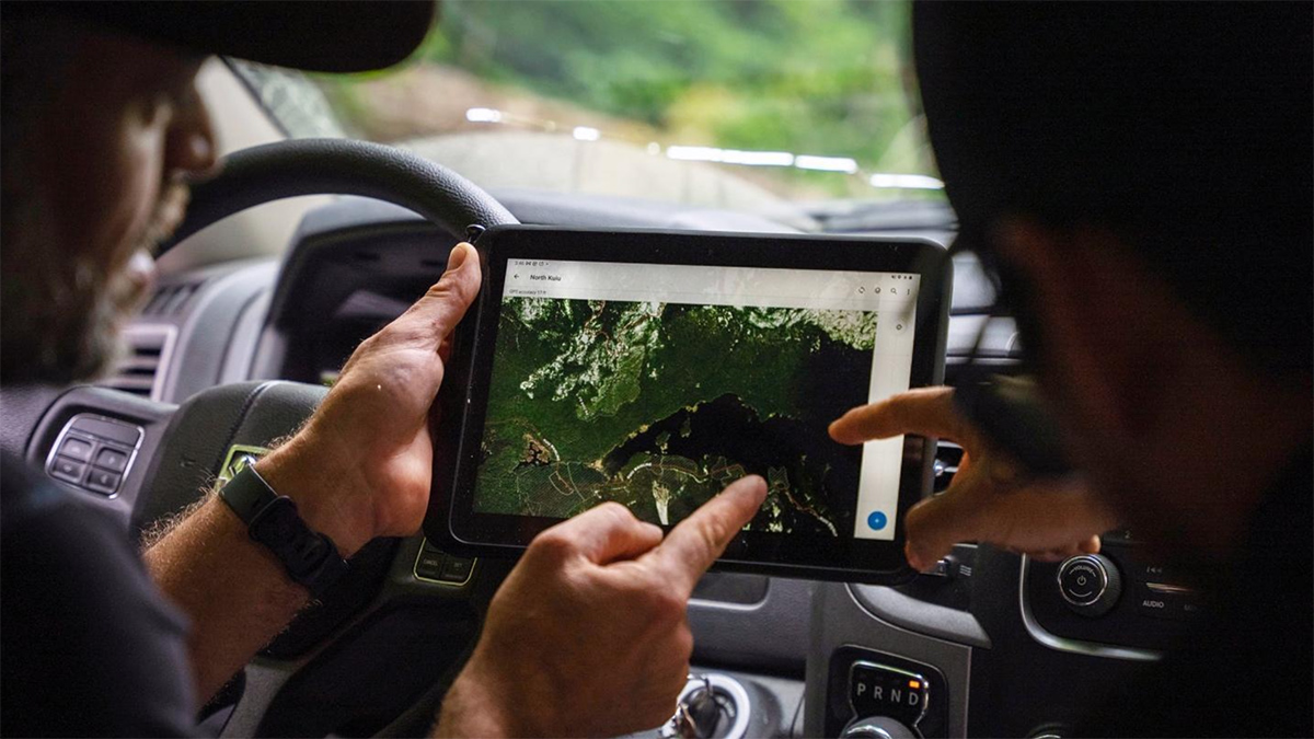 Two people sitting in a car point at an electronic tablet that depicts a map.
