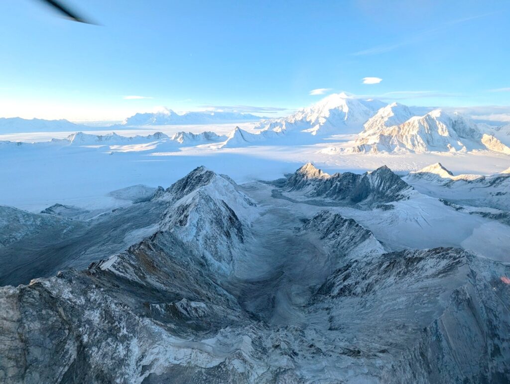 Landslide scars and debris on the NW end of the King George massif, looking toward Mt Logan (5959 m). Note the lack of snow cover here due to concentrated avalanche and landslide activity, as compared to distant peaks.