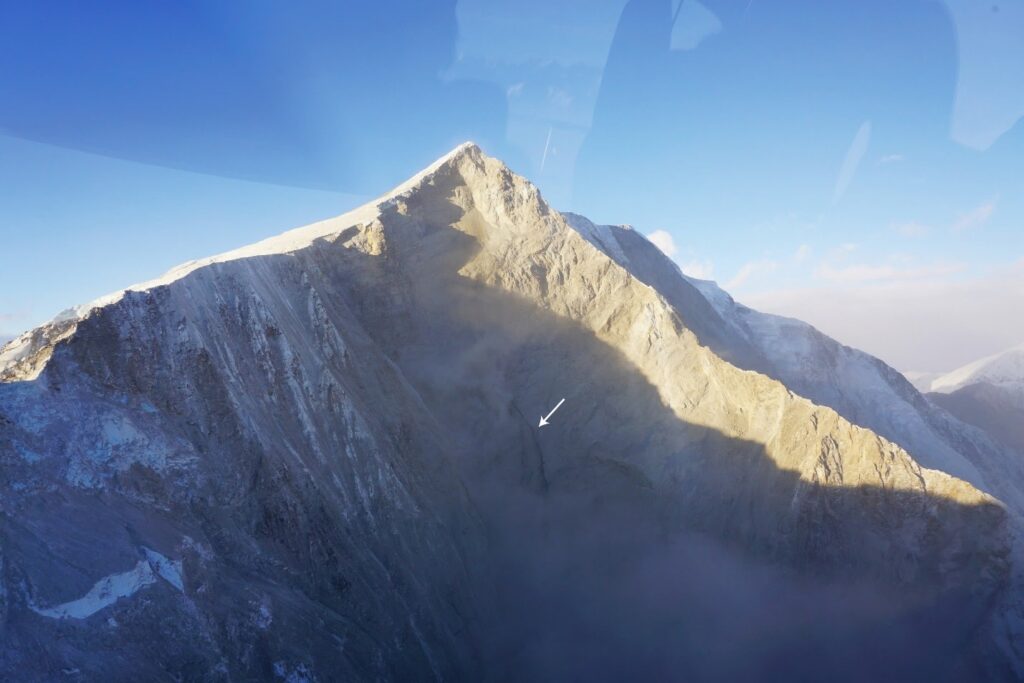 A large landslide scar on the east face of Mt King George appeared to have liquid water running out from approximately halfway down the scar (arrow). This scar was producing active rockfall at the time of the overview flight and filling adjacent valleys with dust.