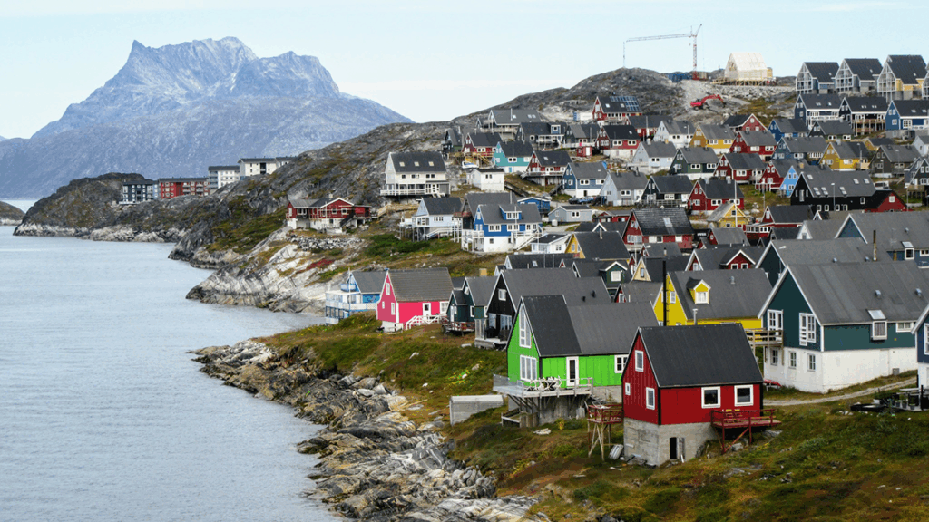 A cluster of colorful house are on a hillside near the ocean. A mountain is visible in the background.