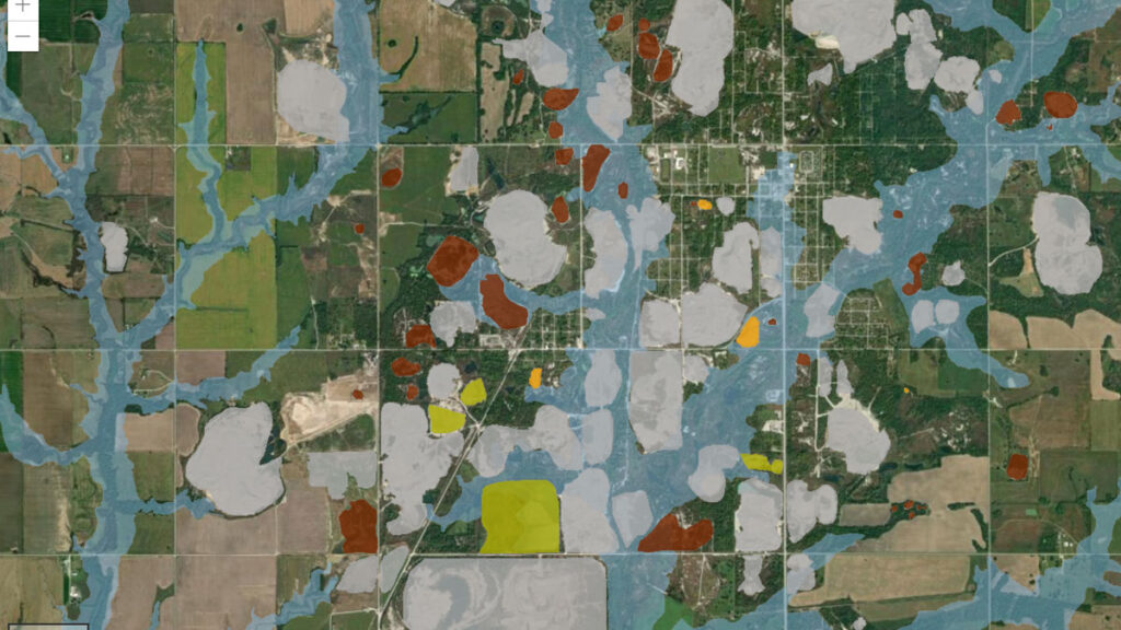 A geographic information system (GIS) map shows a number of different layers: Blue areas represent flood zones or floodways, whereas white areas are those with minimal flood hazard. Red, orange, green, and gray areas represent mining waste.
