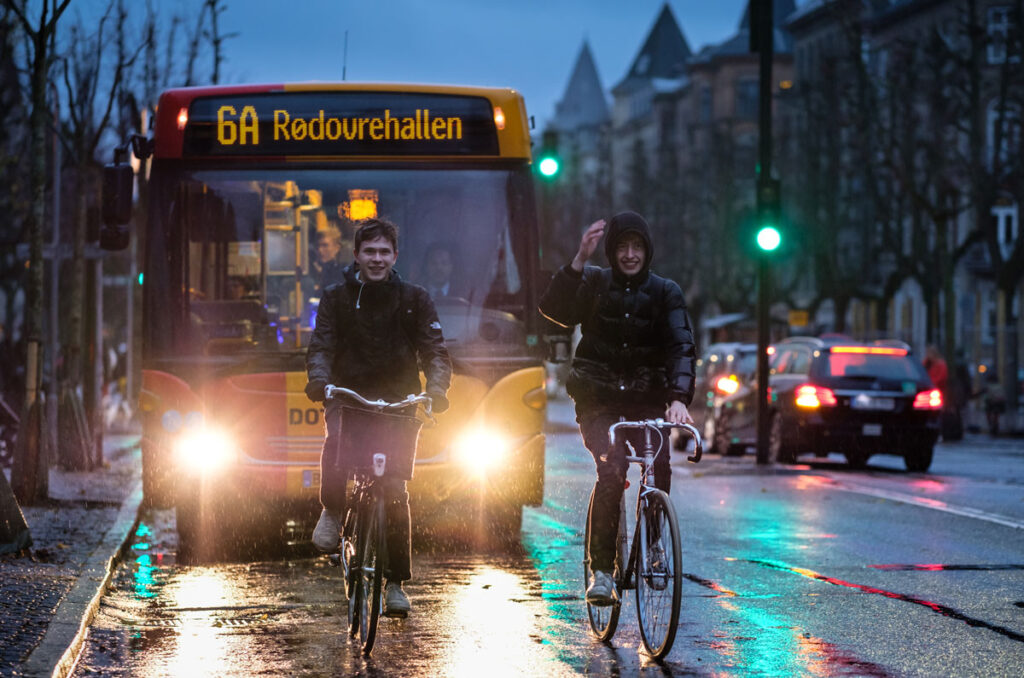 Cyclists and a bus are seen on a rainy night in Copenhagen.