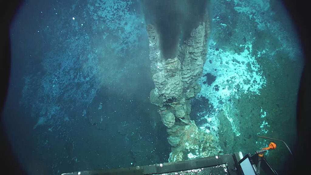A rocky structure on the seafloor has what appears to be black smoke coming out of it.