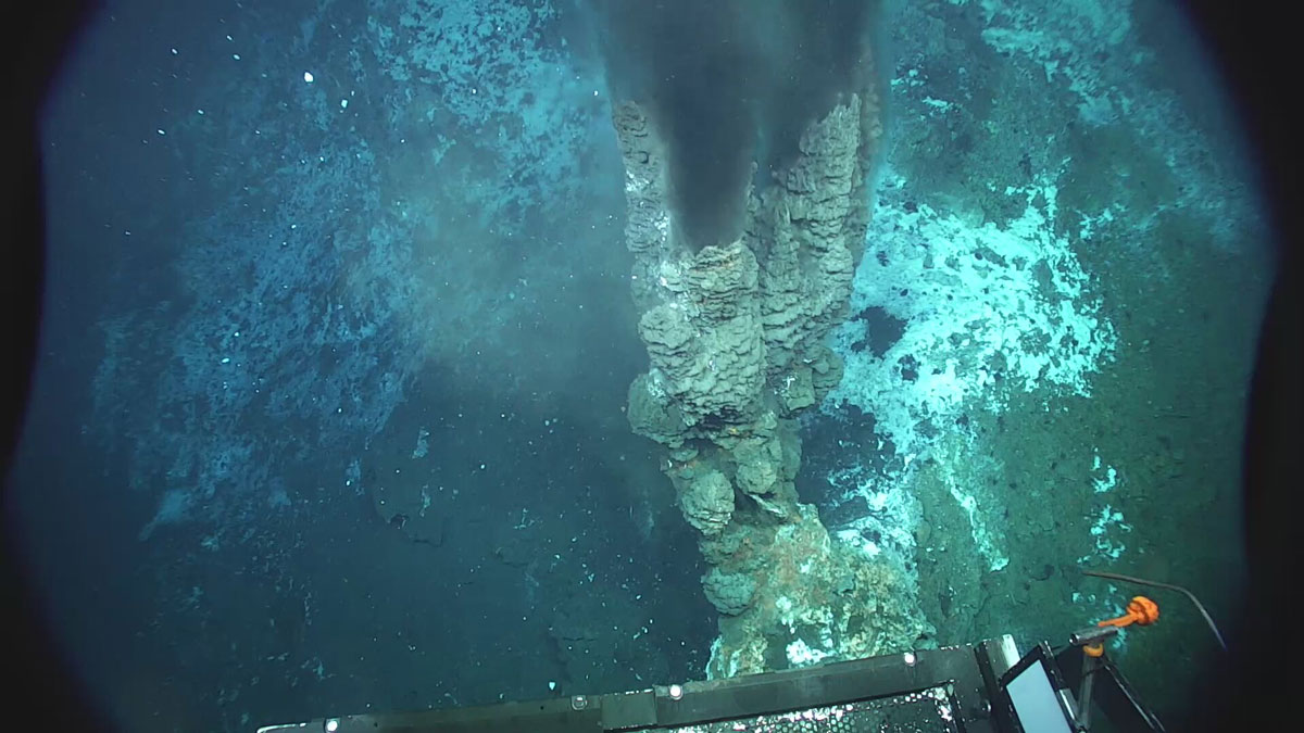 A rocky structure on the seafloor has what appears to be black smoke coming out of it.