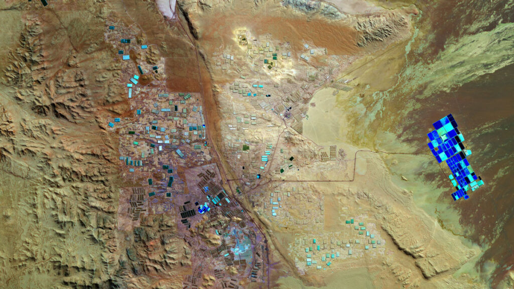 Small, blue, clearly human-made squares are seen from overhead in a brown desert landscape.
