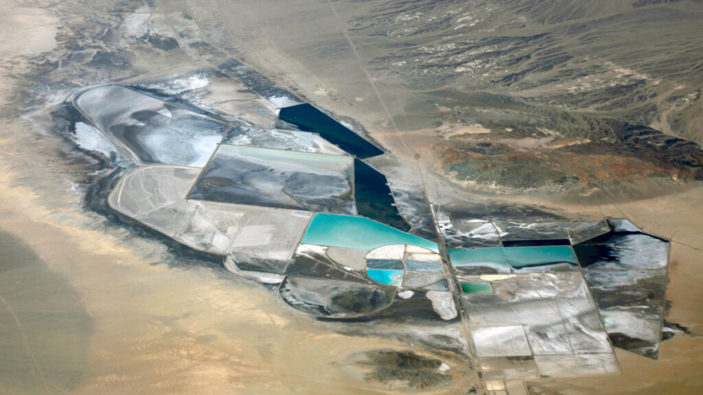 A dry lake bed is seen from overhead. In the middle are a series of circles and round shapes on the ground, some gray and some blue with water.