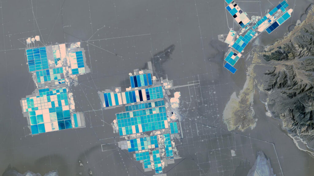 Aerial view of an Atacama lithium mine shows three clusters of large rectangular evaporation ponds in shades of blue, teal, and pink scattered across a gray salt flat.