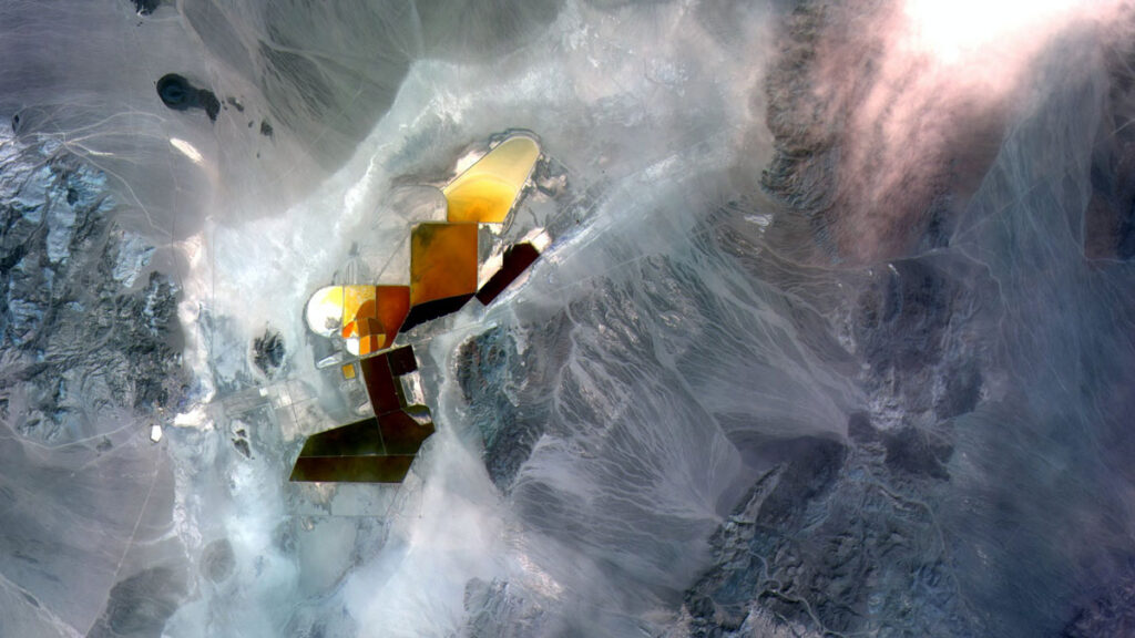 Orange, reflective pools of brine, surrounded by a bluish landscape, are seen from overhead.