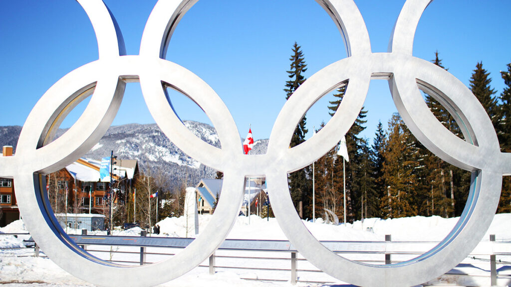 A snowy landscape in Italy is seen through a large statue of the five interlocked Olympic rings.