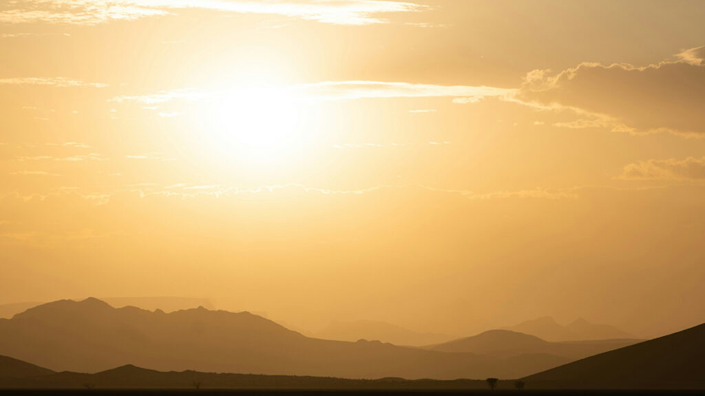 The setting Sun over a mountainous landscape colors the sky in shades of orange.