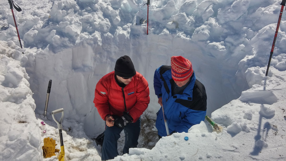 Researchers stand in a round, shoulder-high hole in the snow.
