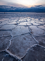 Lavender-gray salt flats extend into the distance, where snow-topped mountains rise into gray clouds.