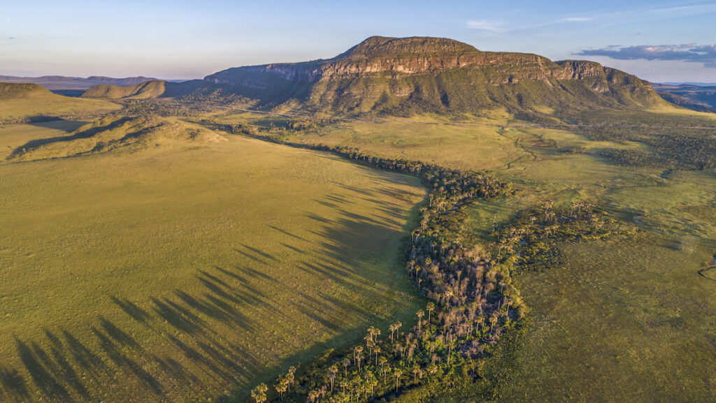 An aerial photo shows a green landscape with a large rock formation in the distance at sunset.