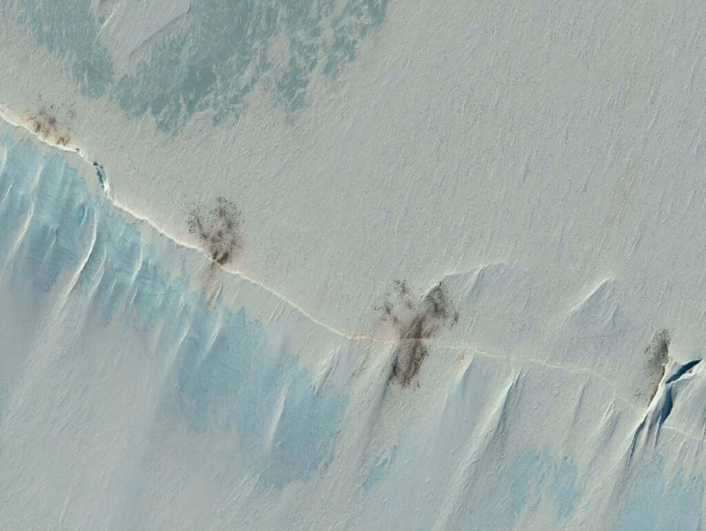An overhead satellite view of Antarctic sea ice show four patches of brown ice in a row.