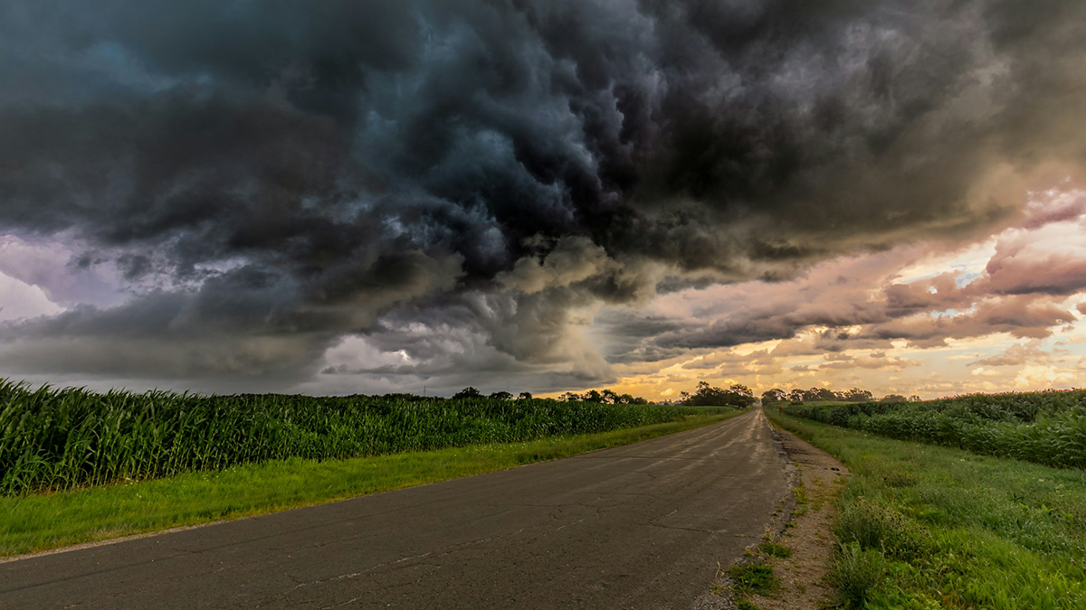 Dark storm clouds looming over a road and crop fields.