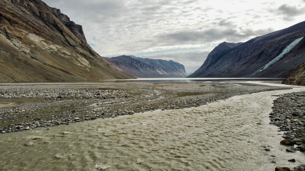 Ground-level view of gray-colored water rippling through a shallow river in a rocky valley between mountains.