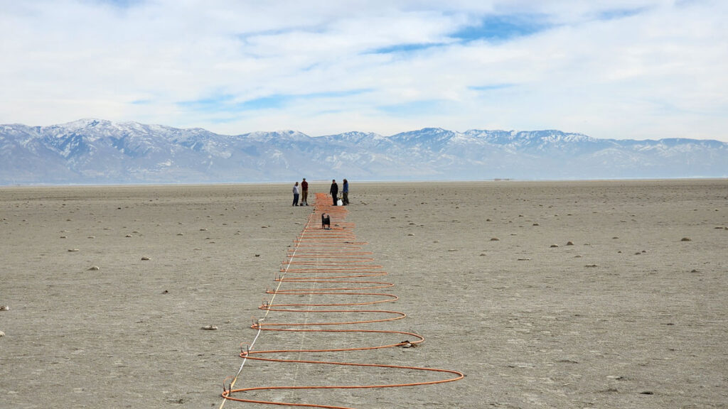 Researchers stand in the distance as an orange electrical cord snakes across a dry lake bed in the Great Salt Lake.