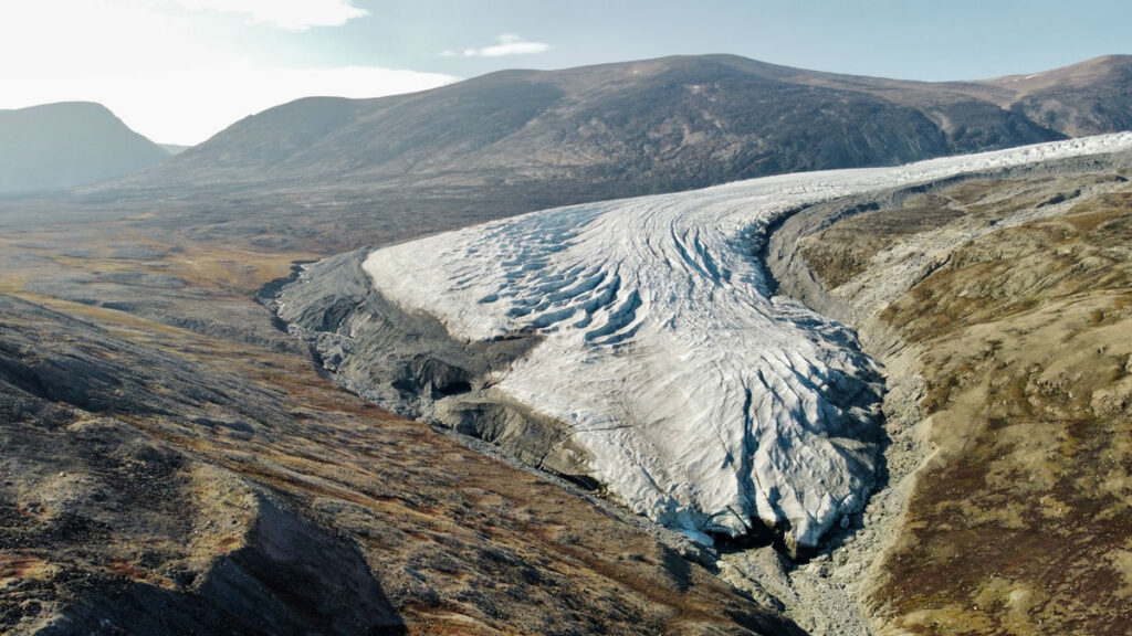A glacial tongue of the Greenland Ice Sheet curves through mountainous tundra.