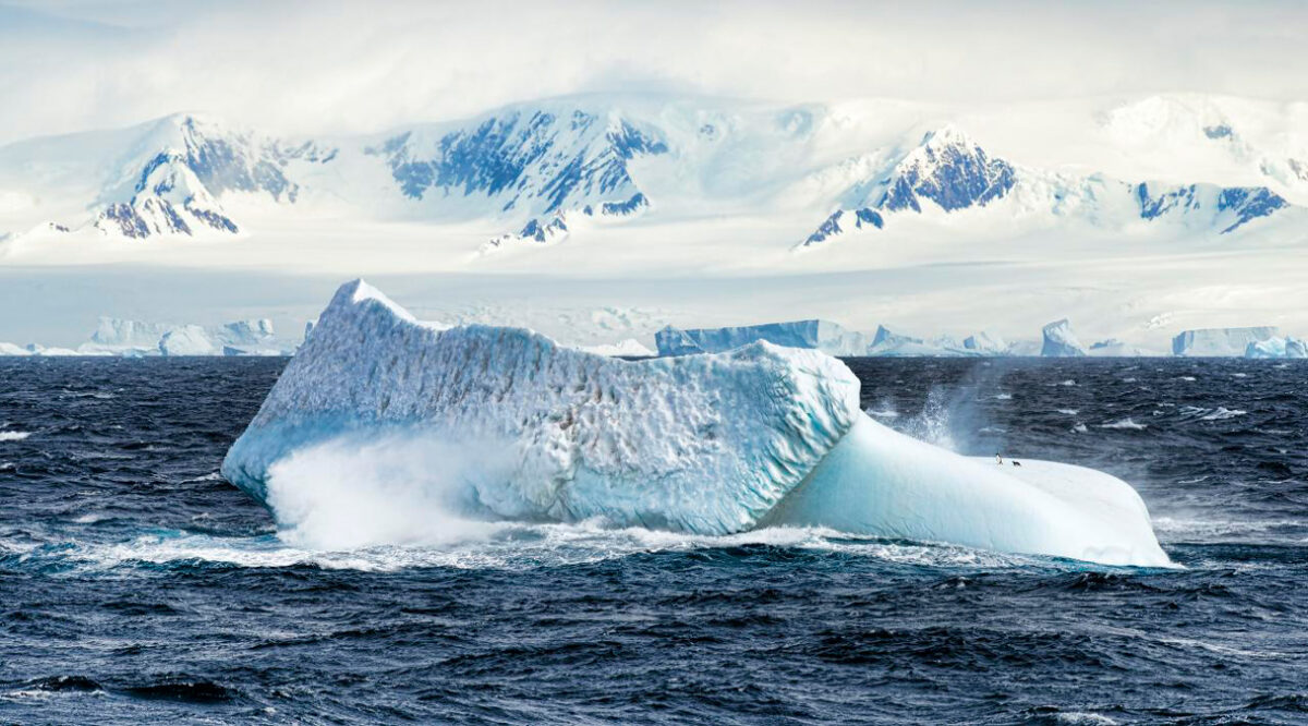 An iceberg sits in a rough, partially frozen sea near Antarctica.