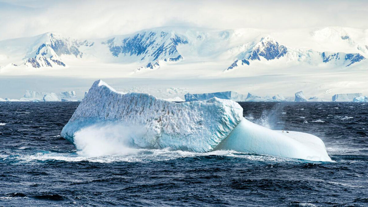 An iceberg sits in a rough, partially frozen sea near Antarctica.