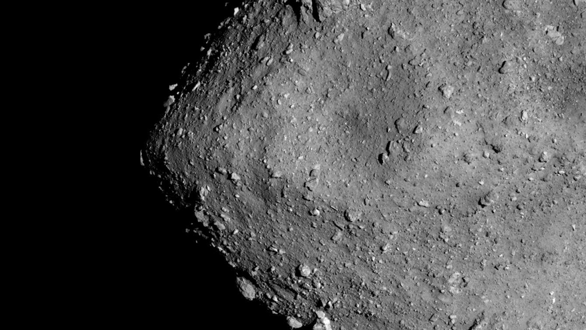 The dusty, dark gray surface of asteroid Ryugu is scattered with boulders and a few craters.