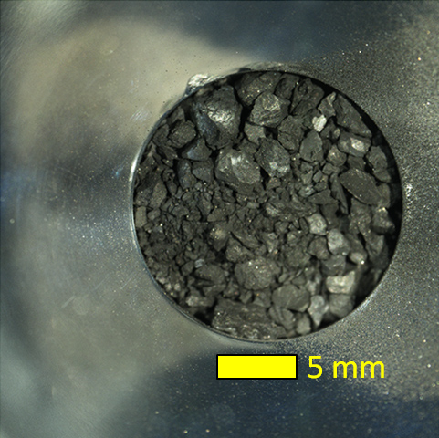 A collection of dark gray grains, with a scale bar showing that the entire sample is only about 2 centimeters across