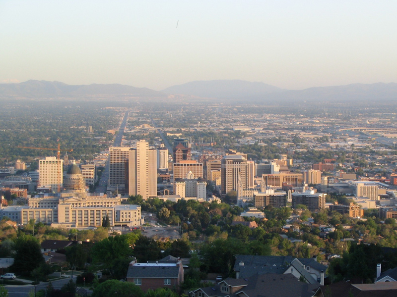 Aerial view of the skyline of part of Salt Lake City, with hazy skies and mountains in the distance.