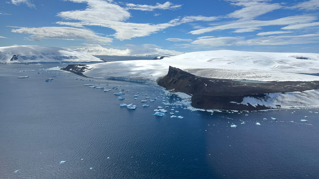 An aerial view of the Southern Ocean and coastline of Antarctica, which is a brown landmass mostly covered in snow