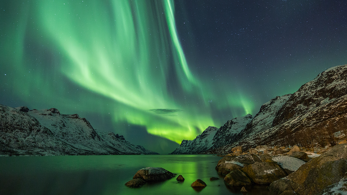 Photo of aurora over a body of water with mountains in the background.