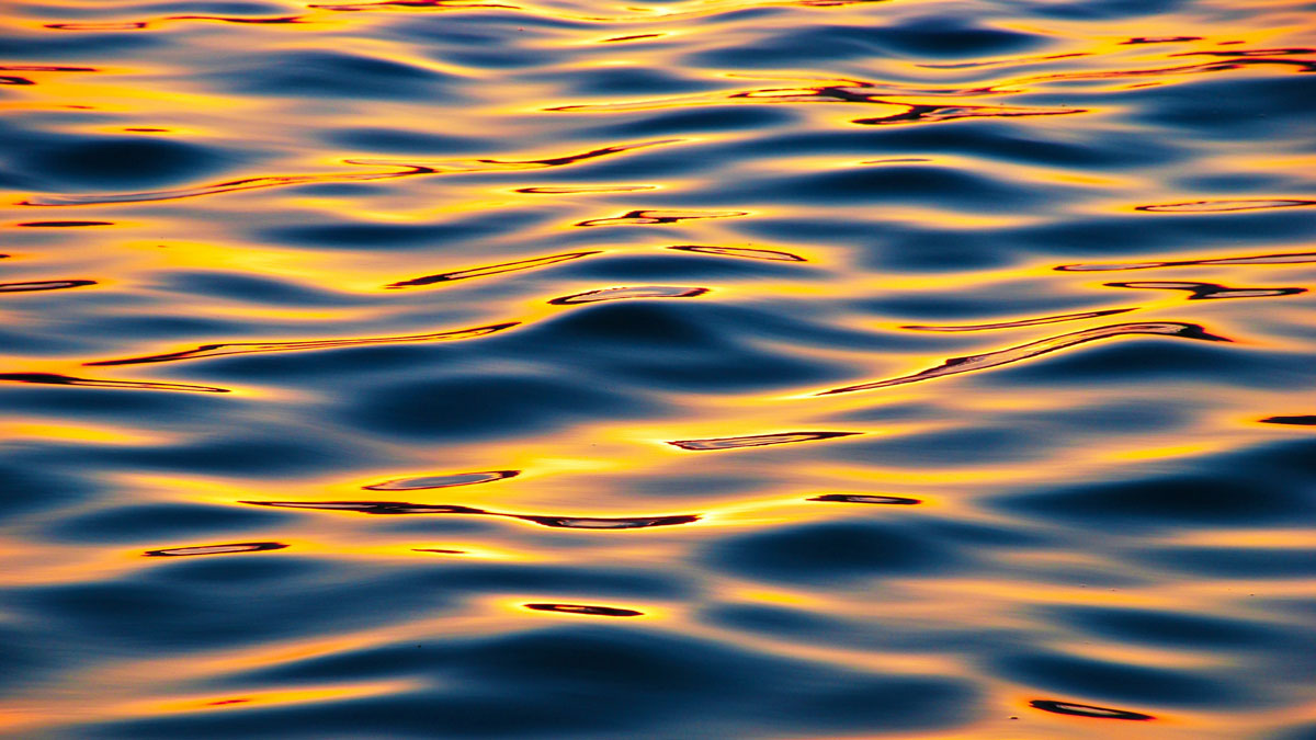 Orange and blue tinted waves with sunlight glinting off the surface.