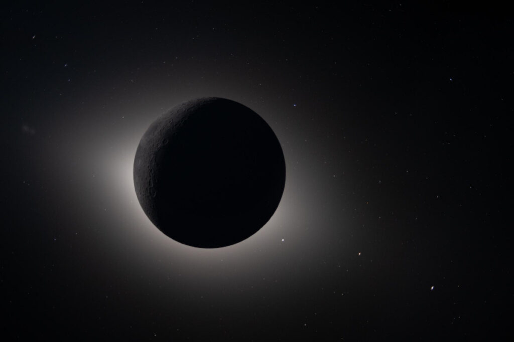 A dark Moon haloed by eclipsed sunlight, with several stars dotted all around.