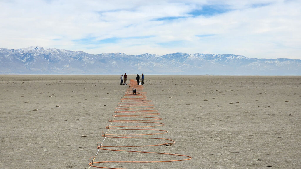 Researchers stand in the distance as an orange electrical cord snakes across a dry lake bed in the Great Salt Lake.