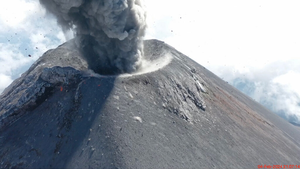 Aerial view of the summit of a volcanic cone as it violently erupts ash and debris.