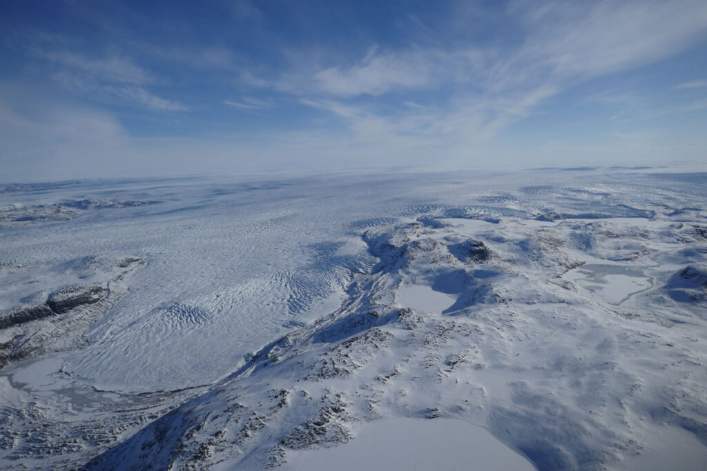 Aerial view of a glacial ice tongue following through a valley between rocky sides.